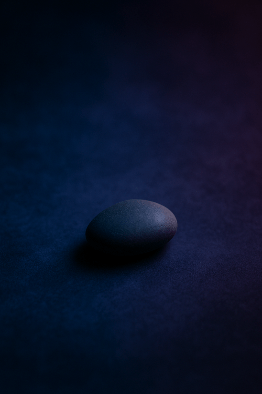 A single smooth stone resting on a dark blue surface—simple, still, existing without needing to mean anything.