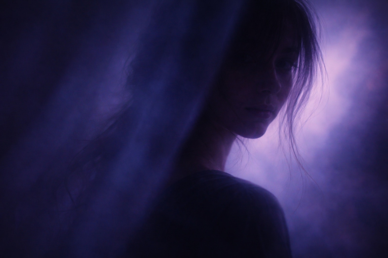 A woman stands in shadow surrounded by purple fog, reflecting on letting people mean what they mean beneath imperfect language.